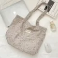 Detailansicht der ästhetischen Blumen-Segeltuchtasche mit Lifestyle-Requisiten auf weißem Grund. - Grau