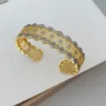 Primo piano dettagliato del largo bracciale rigido in pizzo a nido d'ape con luminosi zirconi. - Bracciale Colore Oro