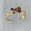 Goldenes Armband mit offener Manschette und einer Schleife aus roten und schwarzen Zirkoniasteinen. - Armreif / Roter Armreif