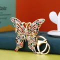 Vista macro di un portachiavi a farfalla dorato ornato con strass colorati vivaci. - Vestibilità regolare / Colori Misti