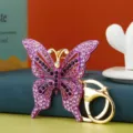 Dettaglio del portachiavi a farfalla con strass viola di lusso e anello dorato. - Vestibilità regolare / Viola