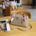 Detalle de bolso caja en cuero genuino, elegante asa con pañuelo y cerradura metálica fina. - Gris Premium