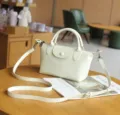 Vista detallada de un bolso cruzado de cuero crema en una mesa de madera de una cafetería. - Blanco Roto