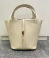 Detailed view of genuine leather bucket bag with lock closure and top handle, elegant style. - Milkshake White with Gold Buckle