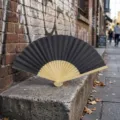 Classic black folding fan with natural bamboo bone ribs on stone street - Style R Plain Satin Fan (Black)