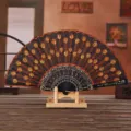 Close-up of black Spanish folding fan with gold sequin peacock tail embroidery on stand - Orange Embroidered Sequin Fan