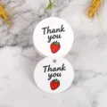 Primo piano di etichette regalo rotonde bianche con grafica di fragola e scritta di ringraziamento. - Stile Fragola (LH-334) / Confezione da 100