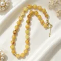 Exquisite amber beaded necklace detail showing golden spacer beads on soft white silk background. - Amber