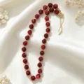 Detailed view of a chic red acrylic bead necklace with gold spacers on white silk. - Red