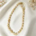 Detailed shot of the elegant acrylic beaded necklace featuring gold metal spacers and charm. - Yellow and White