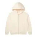 Zip hoodie detail view showing cream fabric texture, zipper, and pocket construction clearly. - Apricot