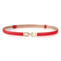 Close-up van de dunne rode lederen damesriem met gouden metalen sluitinggesp detail. - Rood