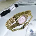 Close-up view of a vintage gold quartz watch with a pink oval rhinestone dial and metal strap. - Gold & Pink