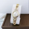 Close-up detail of women's gold quartz watch featuring sparkling rhinestones and clear dial. - White