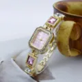 Goldene rechteckige Quarzdamenuhr mit rosafarbenem Zifferblatt, Strasslünette und buntem Armband. - Rosa