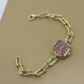 Detailaufnahme einer vergoldeten Quarzuhr mit rotem quadratischen Zifferblatt und Gliederarmband. - Rot