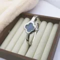 Vue détaillée de l'élégante montre jonc à quartz trèfle à quatre feuilles scintillante. - Noir-Argent