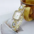 Detailansicht einer eleganten goldenen Quarzuhr mit funkelnden Strasssteinen und Kristallgliedern. - Weiß