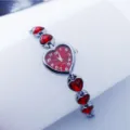 Close-up detail of a red heart crystal quartz watch with metal chain strap for women. - Silver Red