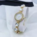 Elegant gold women quartz watch with rhinestone bezel and beaded bracelet chain detail. - White