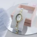 Vista detallada de un elegante reloj pulsera de cuarzo ovalado dorado con brillantes. - Blanco