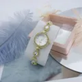 Close-up detail of luxury women rhinestone quartz watch with elegant clover bracelet links. - White