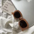 Detailansicht modischer dicker quadratischer Sonnenbrille in Braun auf weißem Stoff. - Braun