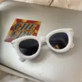 Nahaufnahme der trendigen weißen klobigen Sonnenbrille mit dunklen Gläsern und goldenen Details. - Weiß