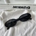 Nahaufnahme einer trendigen schwarzen ovalen Sonnenbrille auf weißem Stoff, minimalistisch. - Kleiner quadratischer Stil / Schwarz