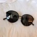 Detaillierte Nahaufnahme stilvoller schwarzer runder Oversize-Sonnenbrille mit goldenem Steg. - Runder Metallrahmen in Schwarz