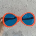 Nahaufnahme von riesigen Party-Sonnenbrillen mit orangen Rahmen und blauen Gläsern als Requisite. - Riesiges Oval / Orange