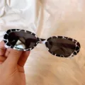 Retro Ovale Sonnenbrille mit modischem Schwarz-Weiß Kuhmuster-Rahmen und dunklen Sonnenschutzgläsern. - Kleine abgerundete Quadrate mit Kuhmuster