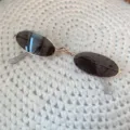 Nahaufnahme von Vintage Mini-Metallsonnenbrille mit ovalen dunklen Gläsern auf Strick. - Kleine ovale Brille mit Goldfassung und schwarzen Gläsern