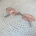 Nahaufnahme von retro Mini-Metallsonnenbrille mit ovalen Gläsern auf Strickgrund. - Kleine ovale Brille mit Silberfassung und rosa Gläsern