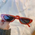 Rote Katzenauge Sonnenbrille Variante mit retro Dreiecks-Kleinrahmen und dunklen Gläsern. - Metallring transparent rot