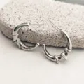 Gros plan de boucles d'oreilles créoles argentées au design unique de croissant de bambou. - Argent