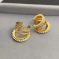 Gros plan détaillé de boucles d'oreilles multicouches dorées avec zircons et perles. - Pièce Unique / Or