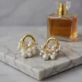 Gros plan de boucles d'oreilles créoles dorées vintage avec perles blanches sur du marbre. - Style de Raisin Vintage (DA260119) / Turquoise Blanche