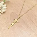 Close-up detail of a gold stainless steel cross necklace with cursive script pendant on wood. - XL1338-10 Gold