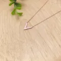 Close-up detail of a minimalist rose gold V-shaped pendant necklace on wooden background. - Rose Gold Necklace - XL1338-01