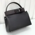 Detail view of the premium genuine leather handbag with chic pyramid stud belt and top handle. - Ebony