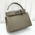 Luxury taupe leather top handle handbag with iconic metal pyramid studs and elegant flap. - Dark Gray