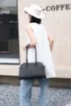 Detail shot of black pebble leather tote bag with long handles in modern urban street scene. - Letter Style / Black