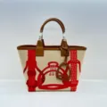 Detail view of the canvas tote bag featuring equestrian motifs and leather top handles. - Totem Red and Brown