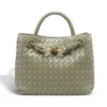 Close-up detail of the woven leather texture and gold knot hardware on the elegant green handbag. - Travertine Green