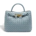 Detailed view of light blue woven leather handbag featuring elegant gold tone knot hardware design. - Fog Blue