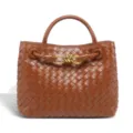 Close-up of brown woven leather handbag detail featuring metal knot hardware and sturdy handles. - Brown