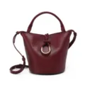Close-up view of the burgundy leather bucket bag featuring a gold ring and braided knot detail. - Burgundy