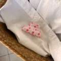 Vue détaillée de la jolie pince à cheveux rose à motif de pommes sur chemise blanche. - Petit Ingot - Pince Pomme Rose Clair
