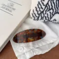 Detailed view of the large tortoise shell pattern spring hair clip featuring gold letter print. - Melon Seed Gold Label Spring Clip / Blue Tortoiseshell